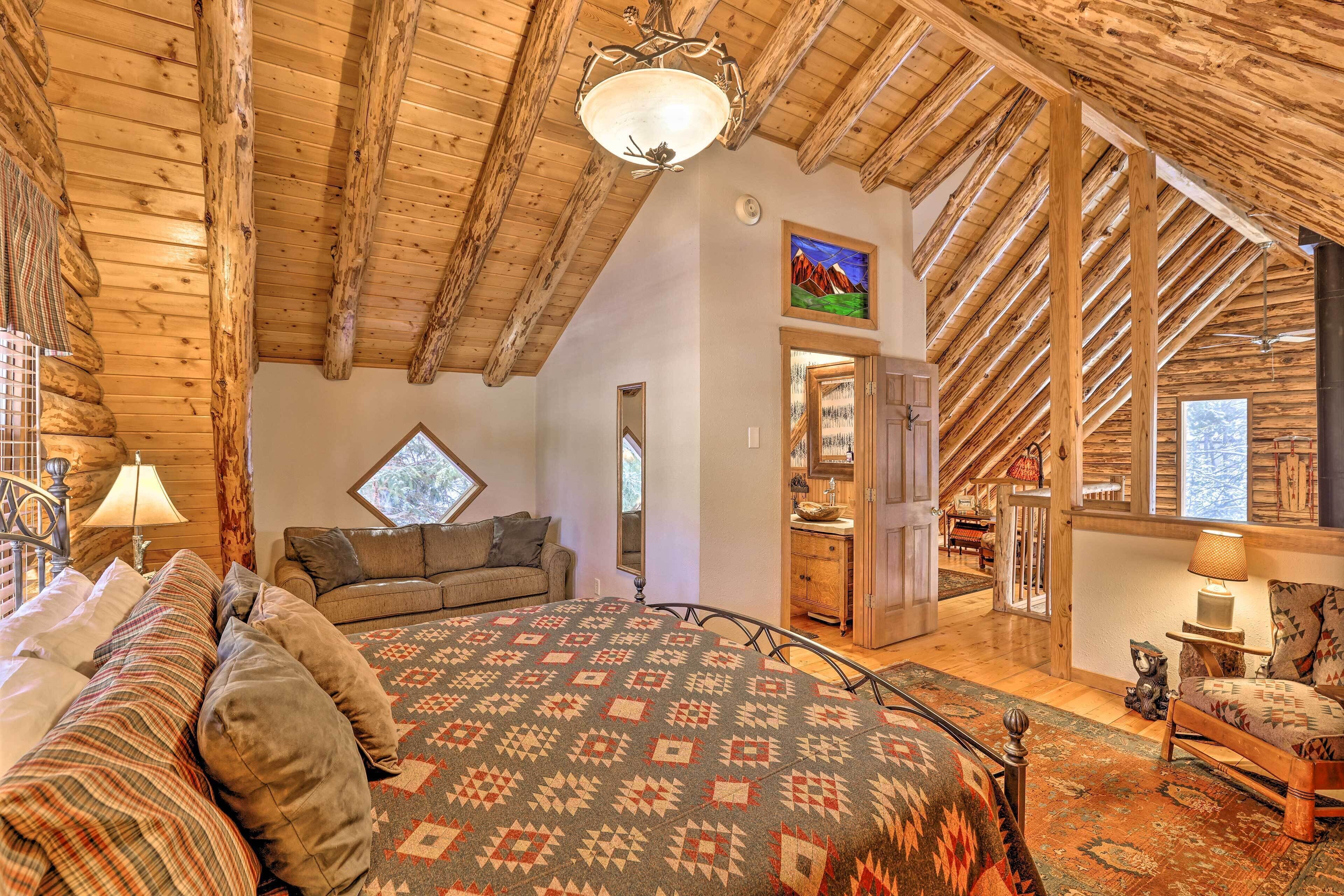 Ein gemütliches Zimmer mit Holzbalkendecke, einem Bett mit gemusterten Textilien, einer Couch und einem Fenster mit Blick auf die Berge.