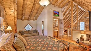 Una habitación acogedora con techo de madera, una cama con ropa de cama estampada, un sofá y una ventana con vistas a la montaña.