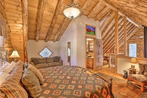 Ein gemütliches Zimmer mit Holzboden, einem Bett mit gemusterten Textilien, einem Fenster und einer Tür zu einem anderen Raum.