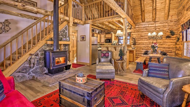 Interior rústico de una cabaña de troncos con chimenea de piedra, escalera de madera y zonas de estar acogedoras.