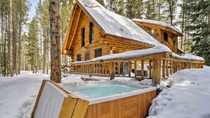 Una cabaña de madera con hidromasaje rodeada de nieve, ubicada en un bosque.