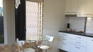 A modern kitchen with white cabinets, a black countertop, and a dining area with a glass table and two chairs. - Holiday at Hillcrest (Scarness)