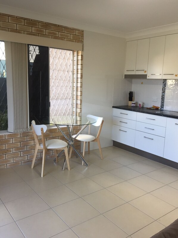 A modern kitchen with white cabinets, a black countertop, and a dining area with a glass table and two chairs.