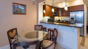 A modern kitchen with wooden cabinets, stainless steel appliances, and a glass dining table with wicker chairs.