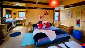 Ein modernes Schlafzimmer mit einem großen Bett, einer Holzbalkendecke und einem durch eine offene Tür sichtbaren Küchenbereich.