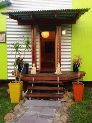 Un edificio con fachada verde, un porche de madera con escalones y dos estatuas de Buda en el porche.