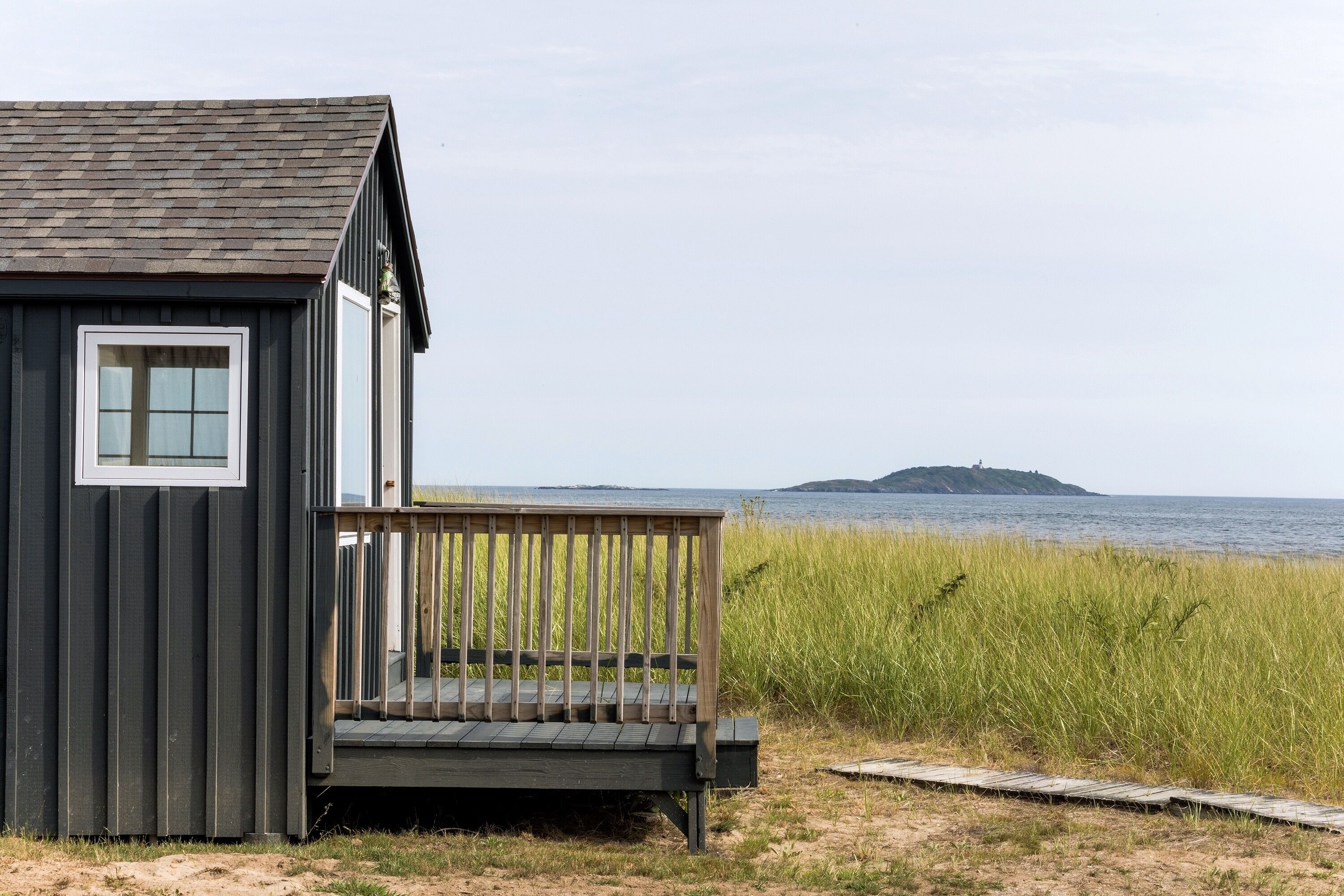 Une petite cabane en bois dotée d’un balcon donnant sur une plage et une île lointaine.
