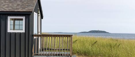 Une petite cabane en bois dotée d’un balcon donnant sur une plage et une île lointaine.