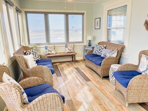Ein gemütliches Zimmer mit Korbmöbeln, einer Sitzbank und Blick durch große Fenster.