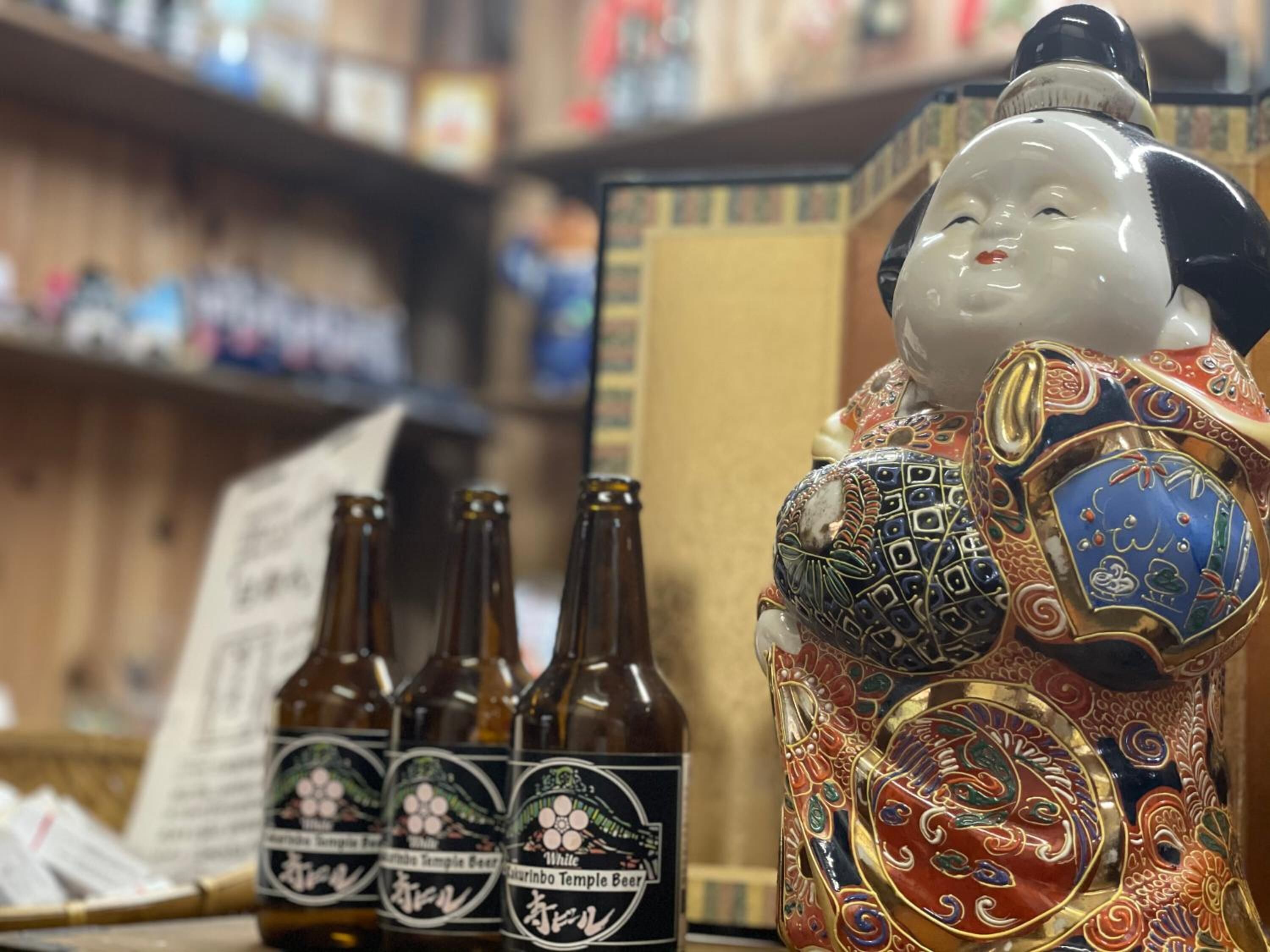 A decorative ceramic figure with intricate patterns and three bottles of beer labeled "Zaruninbo Temple Beer" in front of it.