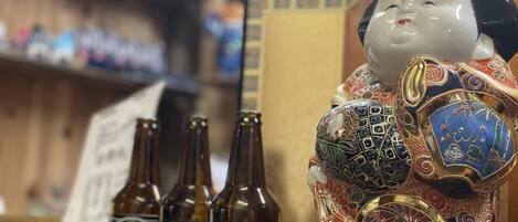 A decorative ceramic figure with intricate patterns and three bottles of beer labeled "Zaruninbo Temple Beer" in front of it.