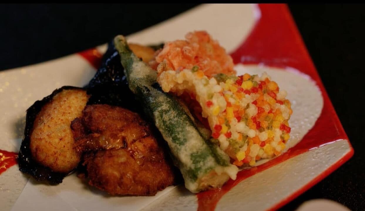 A plate with various dishes including fried items, a rolled vegetable, and a rice-based dish.