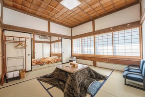 Una habitación japonesa tradicional con suelo de tatami, una mesa baja, un sofá y puertas correderas.