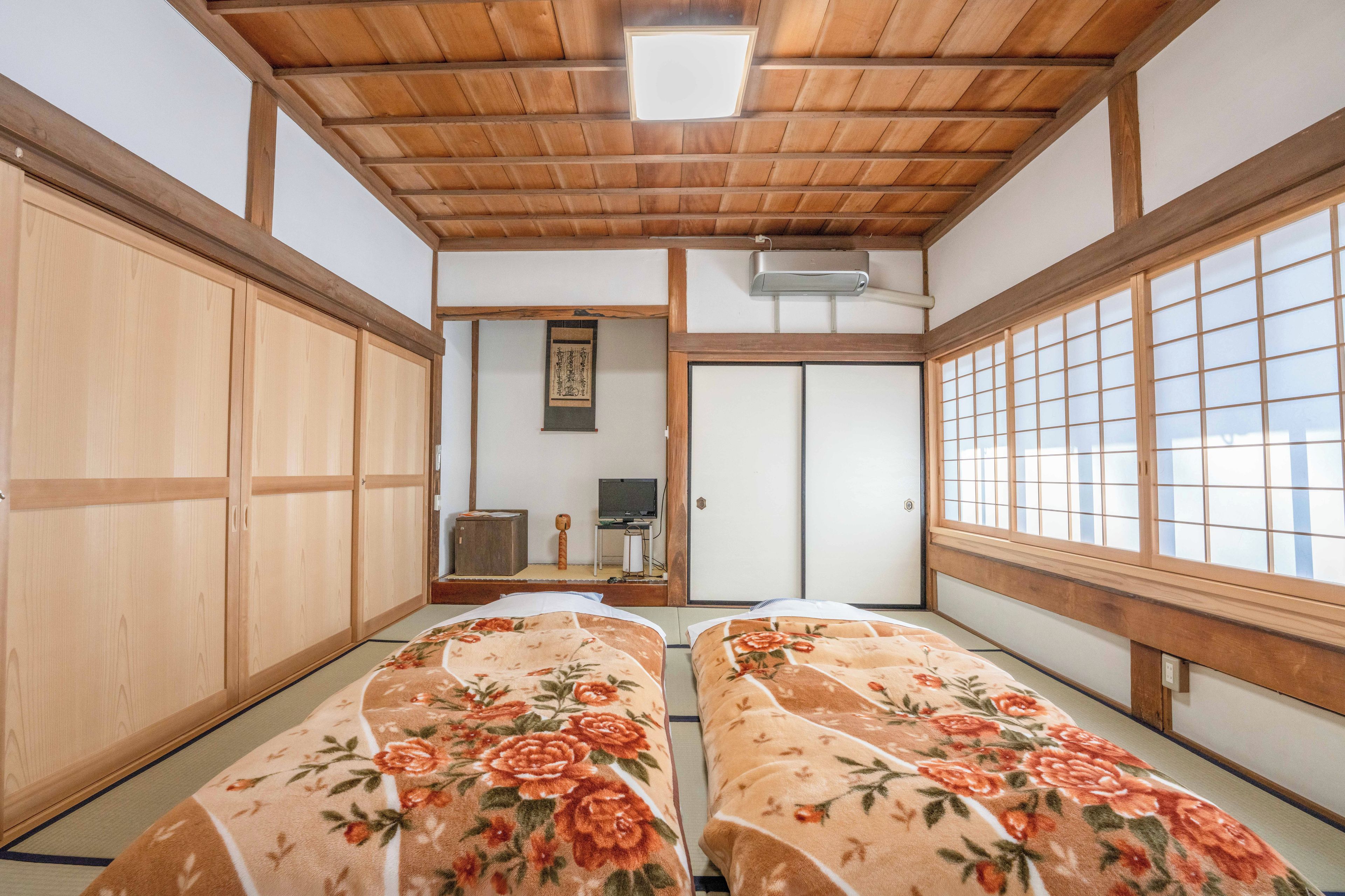 Una habitación tradicional japonesa con suelo de tatami, puertas correderas de madera y una cama con ropa de cama floral.