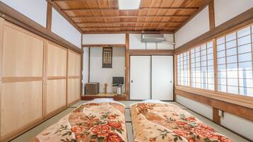 Una habitación tradicional japonesa con suelo de tatami, puertas correderas de madera y una cama con ropa de cama floral.