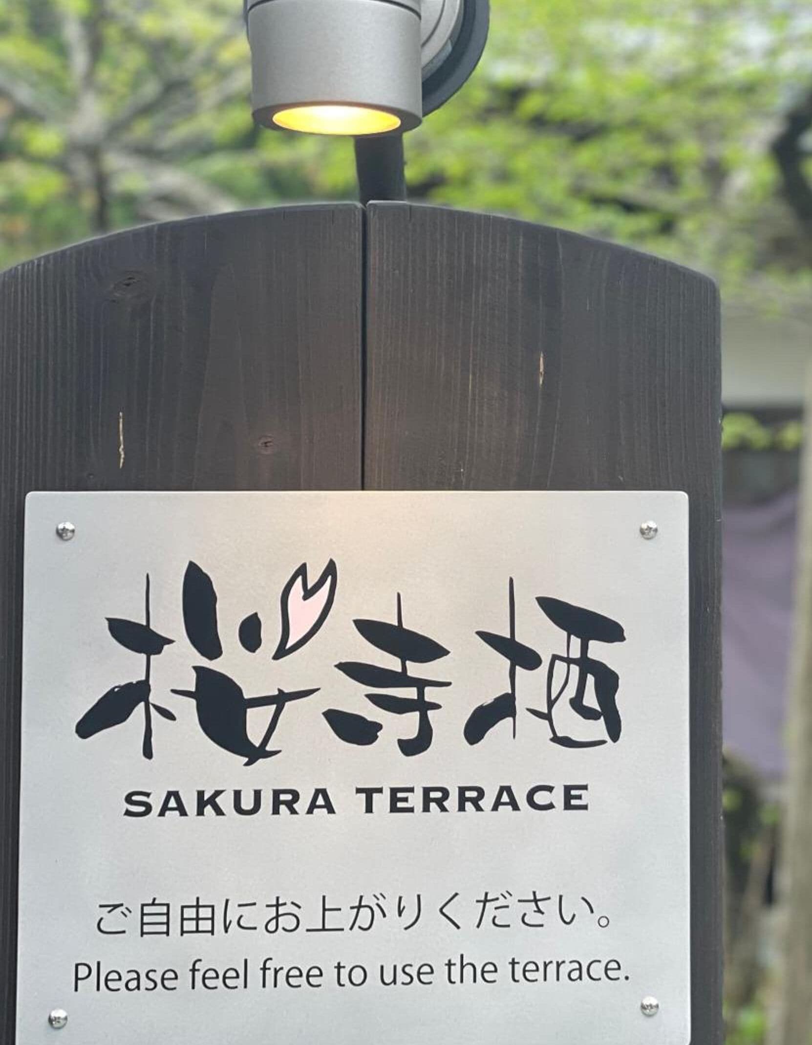 Señal para la Terraza Sakura, con caracteres japoneses y texto en inglés que invita a disfrutar de la terraza.