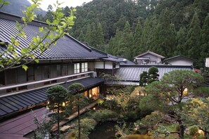 Een traditioneel Japans gebouw met meerdere niveaus, een vijver met koi karpers en een bebost achtergrond.