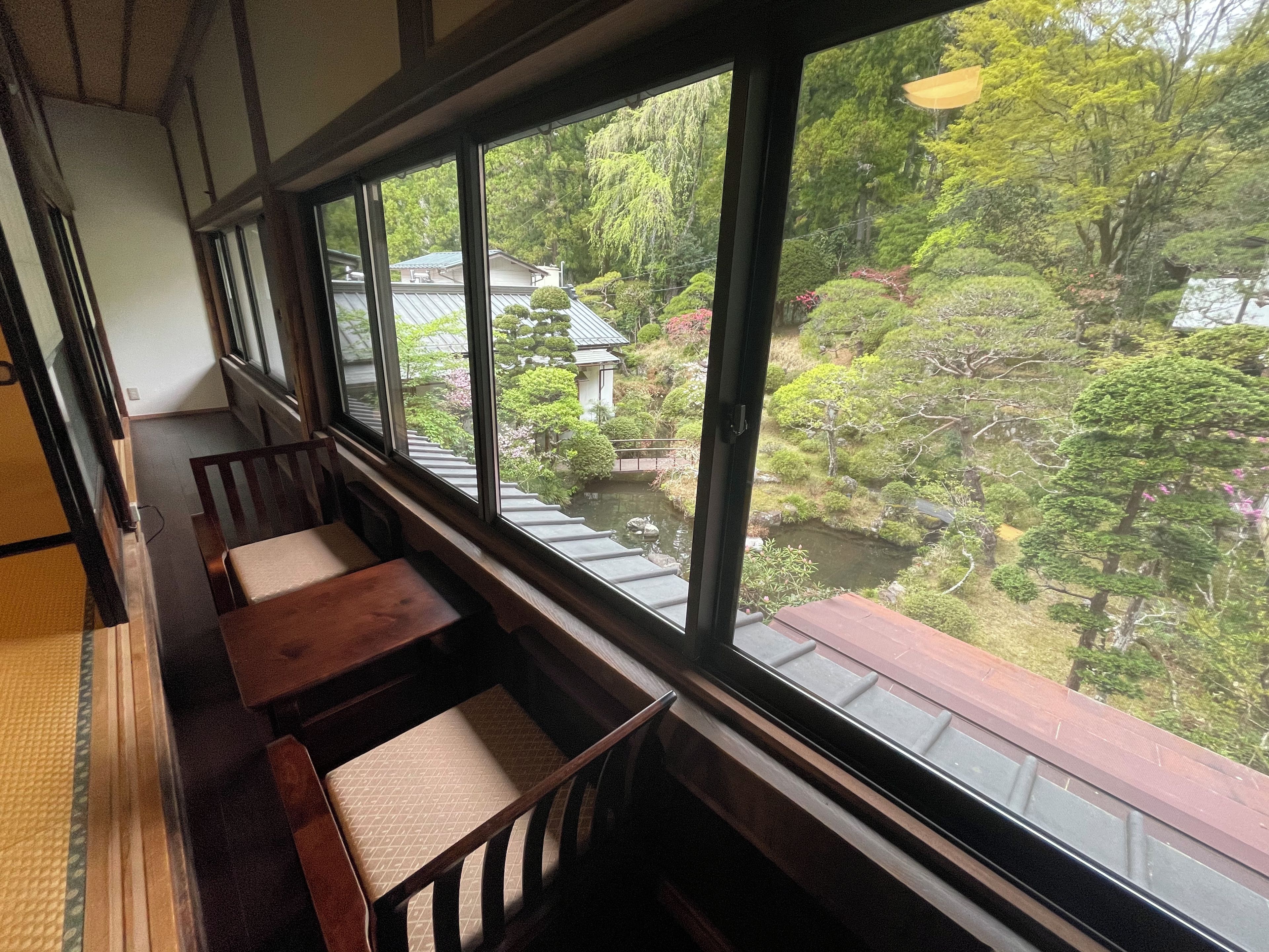 A traditional Japanese-style room with tatami flooring, a low wooden table, and a view of a garden through large windows.