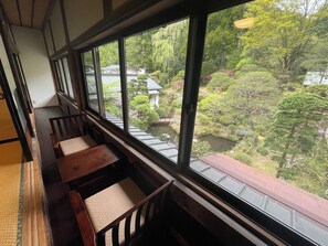 Una habitación tradicional japonesa con suelo de tatami, una mesa de madera baja y vistas a un jardín a través de amplios ventanales.