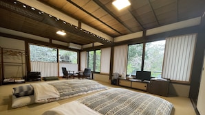 A traditional Japanese-style room with tatami flooring, two beds with patterned bedding, a television, and a desk with a computer. - Shukubo Kakurinbo (Minobu)