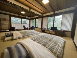 Una habitación tradicional japonesa con suelo de tatami, dos camas con ropa de cama estampada, un televisor y un escritorio con computadora.
