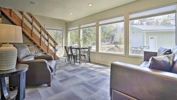 A spacious living area with a staircase, leather sofas, a dining table, and large windows offering a view of the outdoors. - Cabin w/ Hot Tub & Views: 1 Mile to Alyeska Resort (Girdwood)