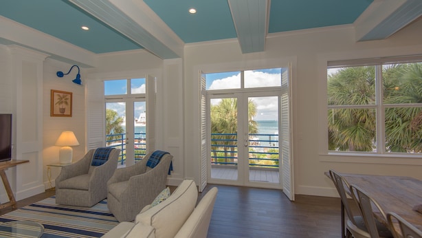 A spacious living room with a view of the ocean, a dining area, and a cozy seating area with a TV and lamp. - A Sunset & Harbour View at The Truman Annex in Key West (Key West)