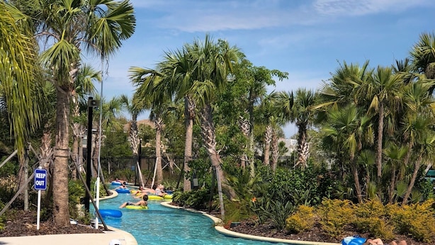 A pool area with clear water, palm trees, and people on inflatable rafts. - Affordable and so close to Disney  Solterra Resort (Davenport)