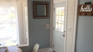 A room with a round table, two chairs, a trash can, a door, and a 'hello' sign on the wall. - Waterfront Cottage, Blue Chair Bungalow, minutes from the beach (South Kingstown)