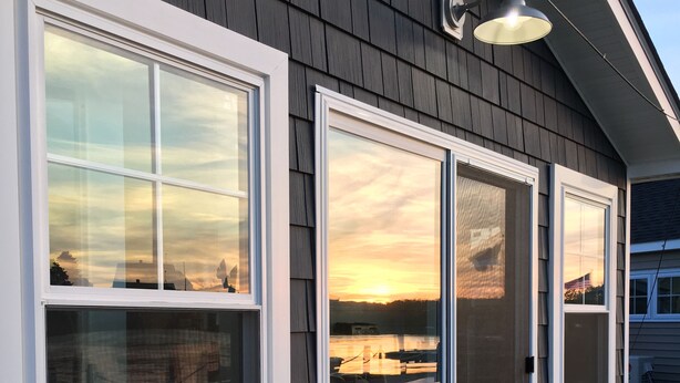 A house with large windows, a porch with steps, and a view of a body of water during sunset. - Waterfront Cottage, Blue Chair Bungalow, minutes from the beach (South Kingstown)