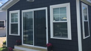 A small, dark-colored house with white trim, a front porch, and two potted plants. - Waterfront Cottage, Blue Chair Bungalow, minutes from the beach (South Kingstown)
