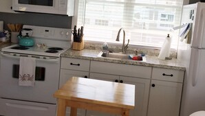 A compact kitchen with white cabinets, a microwave, stove, sink, and a wooden chair. - Waterfront Cottage, Blue Chair Bungalow, minutes from the beach (South Kingstown)