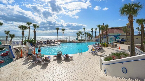 A poolside area with lounge chairs, palm trees, and a view of the ocean.
