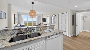 A modern kitchen with granite countertops, stainless steel sink, and white cabinetry.