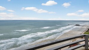 A coastal view with a beach, ocean waves, and a pier extending into the water.