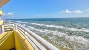 A balcony with a view of the ocean, white railing, and a yellow wall.