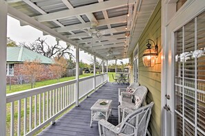 A covered porch with wicker furniture and a table, a brick house in the background, and a fence. - Walk to the Waves! Pass Christian Beach Retreat (Pass Christian)