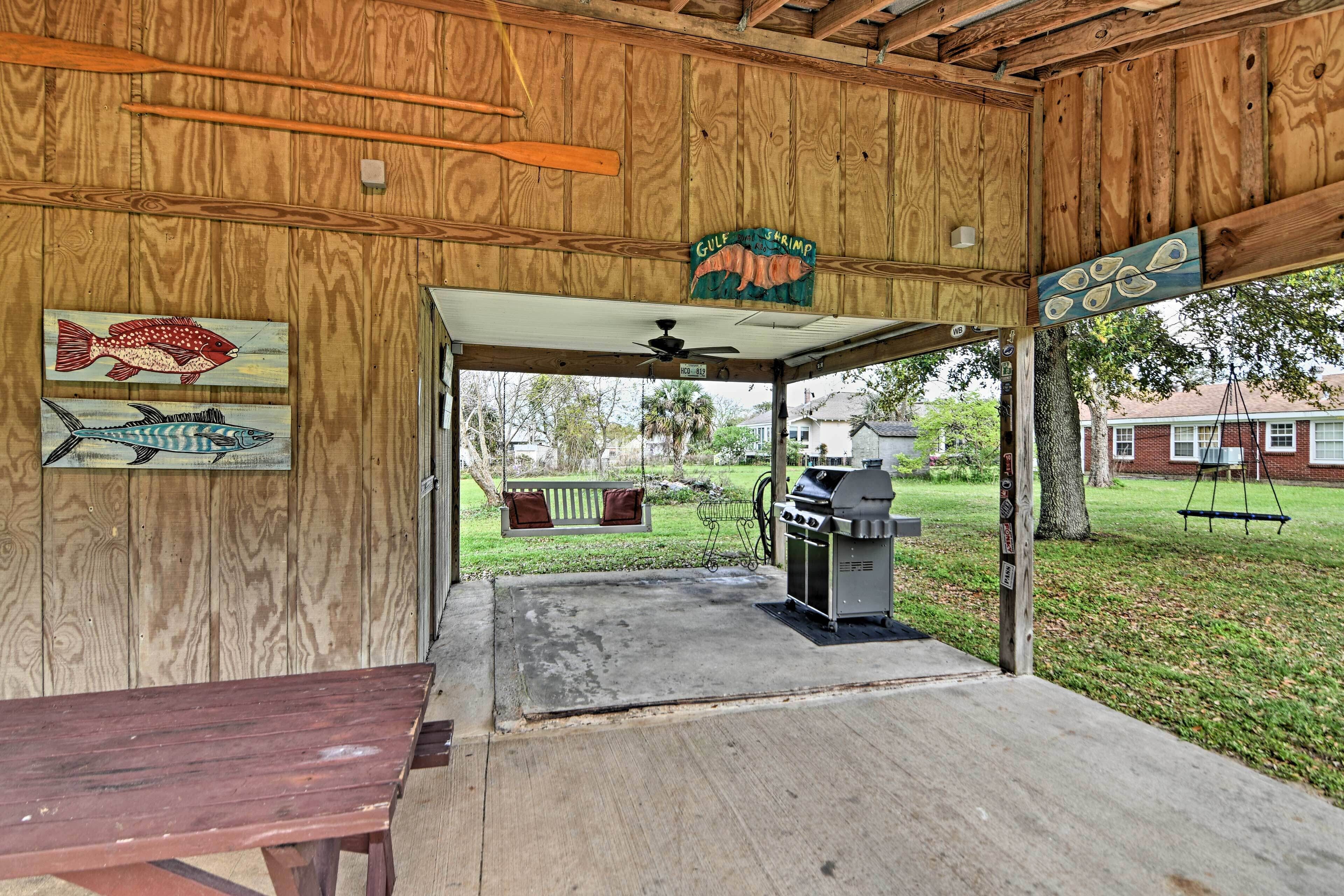 A covered outdoor area with a wooden ceiling, a grill, and a swing set.