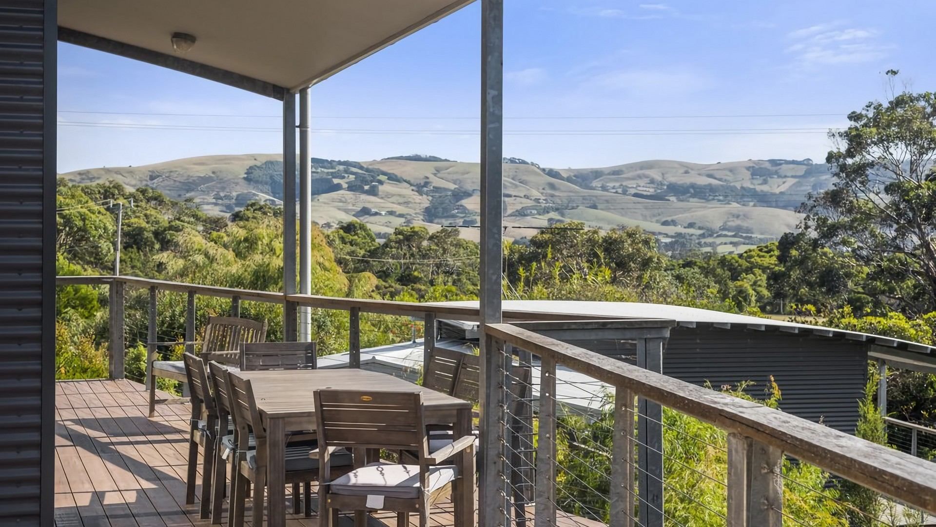 A balcony with a table and chairs, overlooking a hilly landscape.