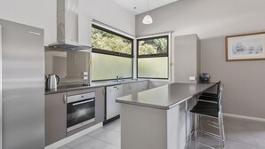 Eine moderne Küche mit Backofen, Edelstahl-Kühlschrank, großem Fenster und einer Bar mit Hockern.