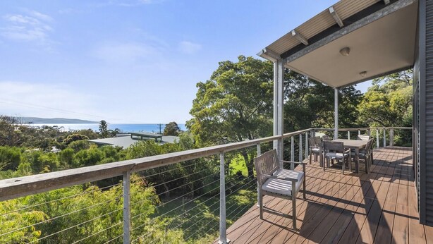Eine Holzdar Terrasse mit Gartenmöbeln, mit Blick auf eine malerische Landschaft mit Bäumen und Meerblick.