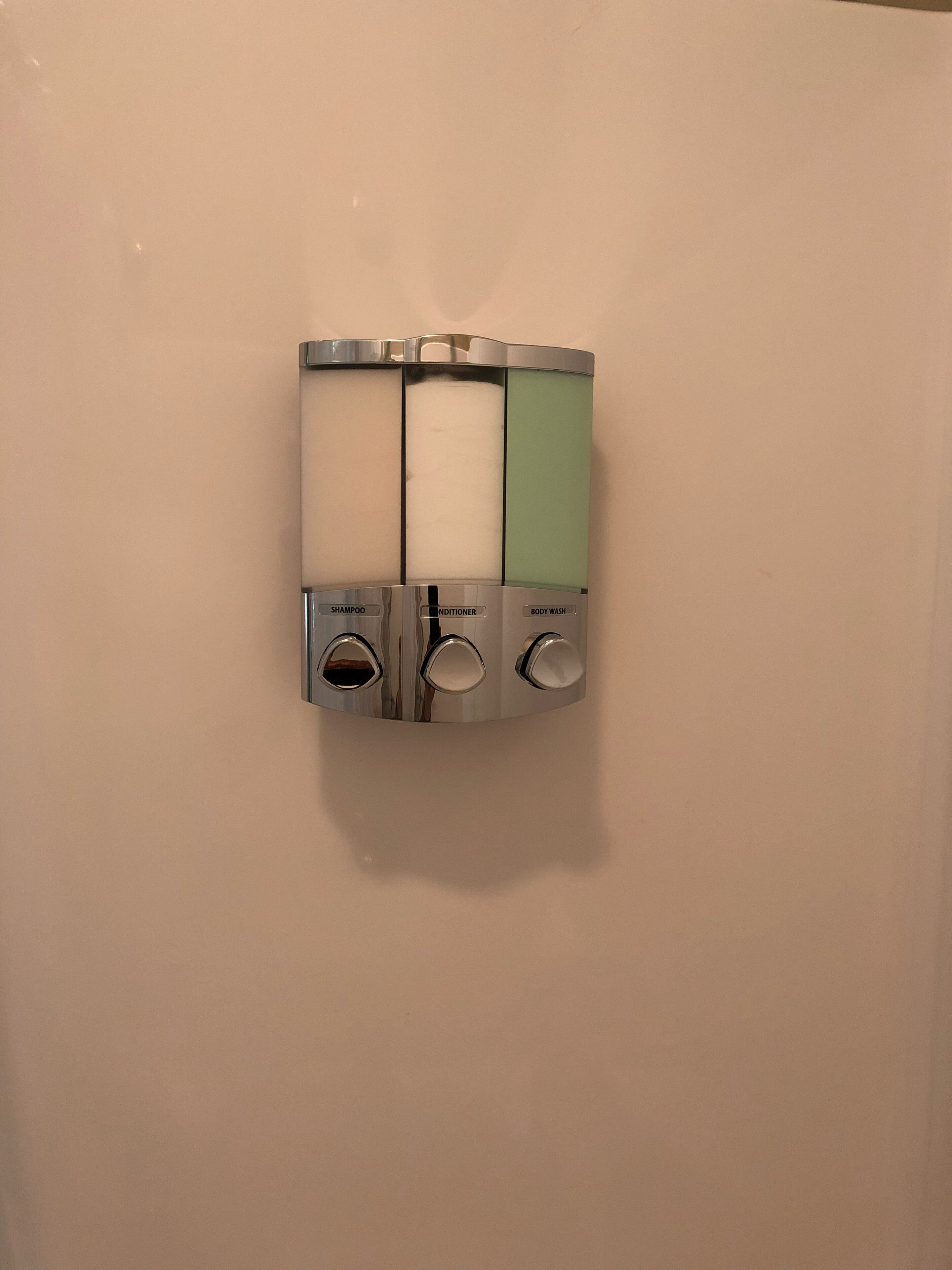 A wall-mounted dispenser with three compartments labeled "shampoo," "conditioner," and "body wash."