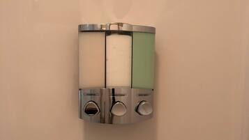 A wall-mounted dispenser with three compartments labeled "shampoo," "conditioner," and "body wash."