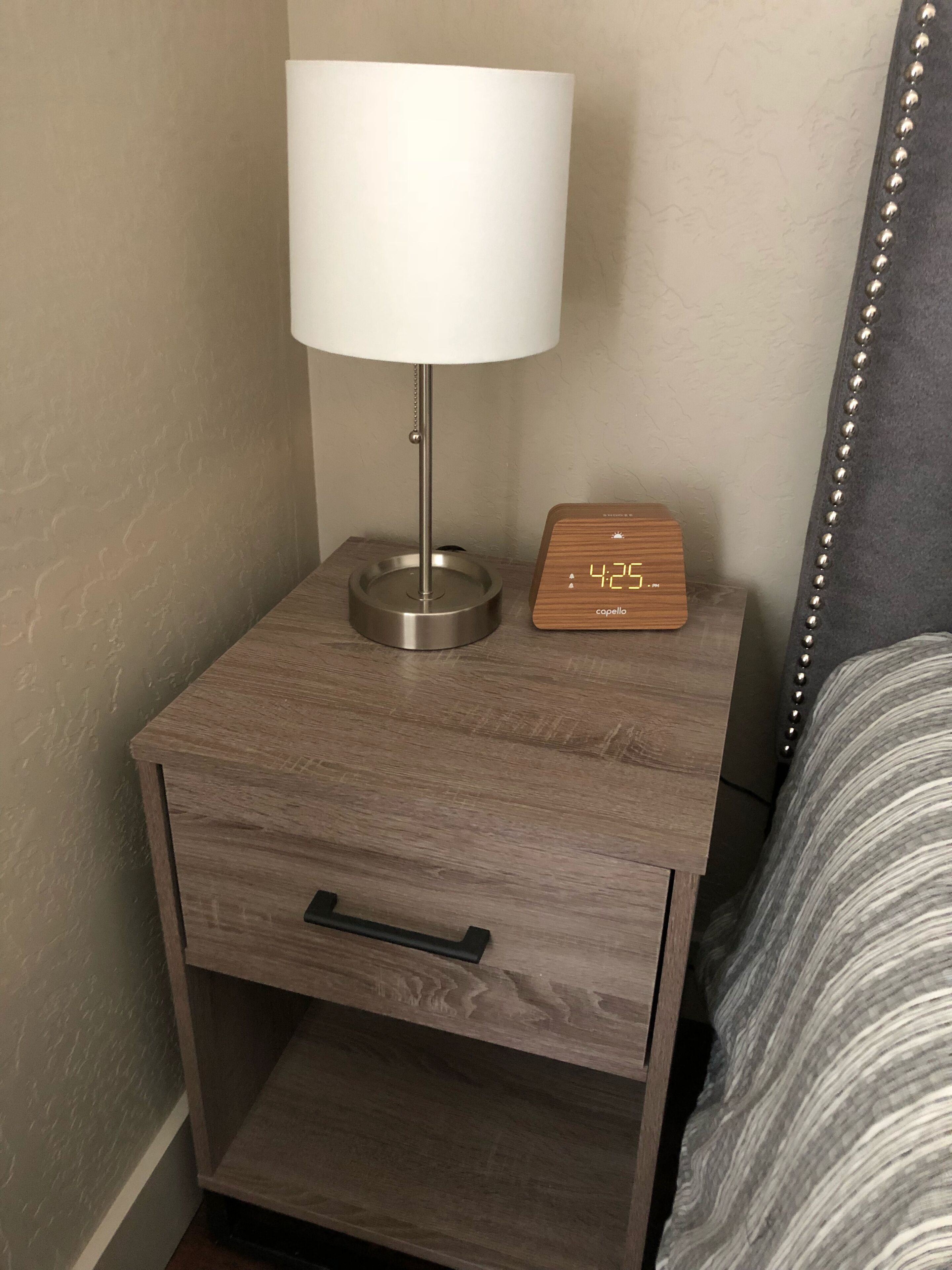 A wooden bedside table with a lamp and a digital clock.