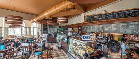 A restaurant interior with checkered flooring, wooden furniture, a cash register, and a menu board.