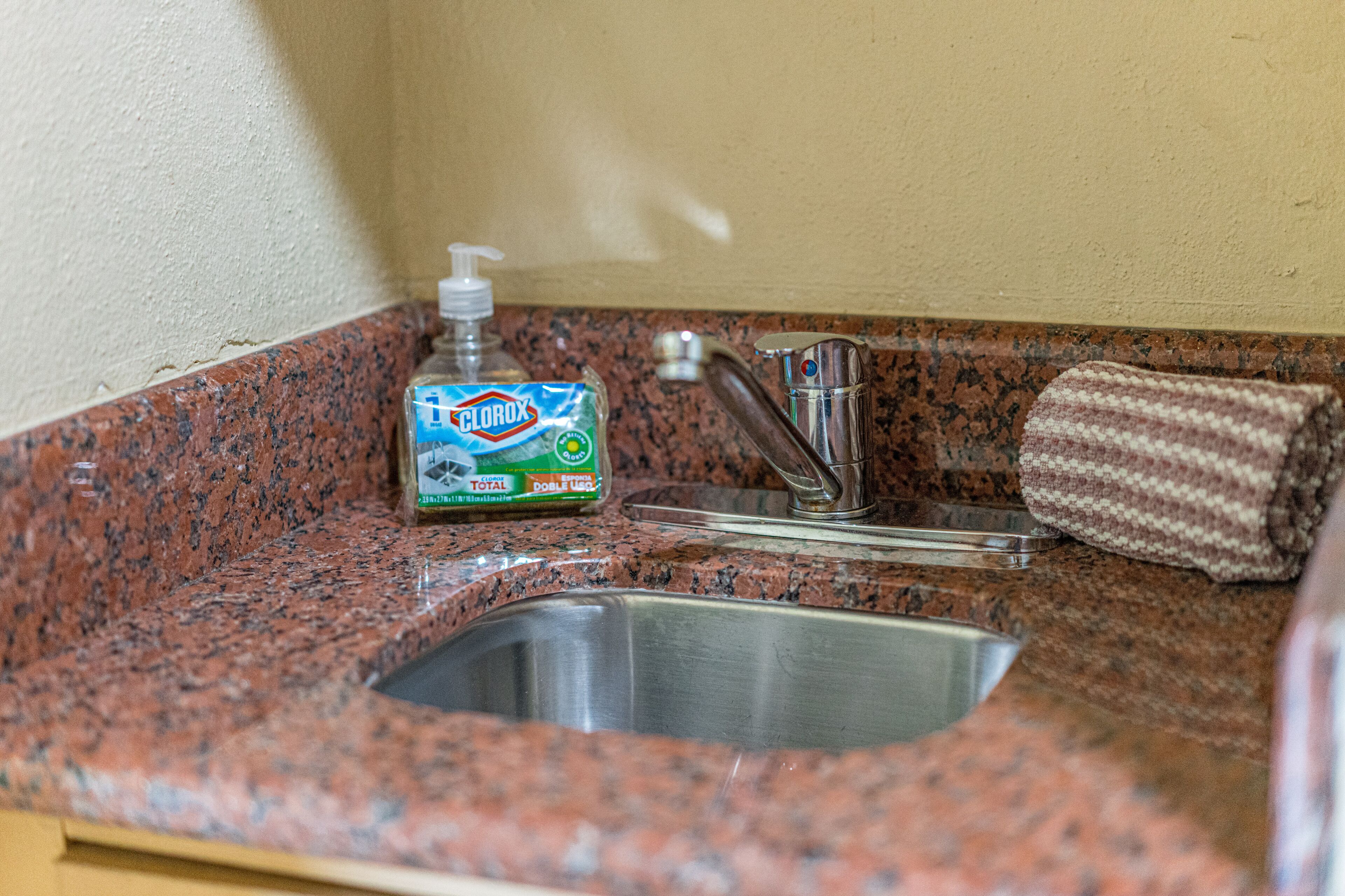 Cozinha com bancada de granito, pia de aço inoxidável e uma garrafa de detergente Clorox Total.