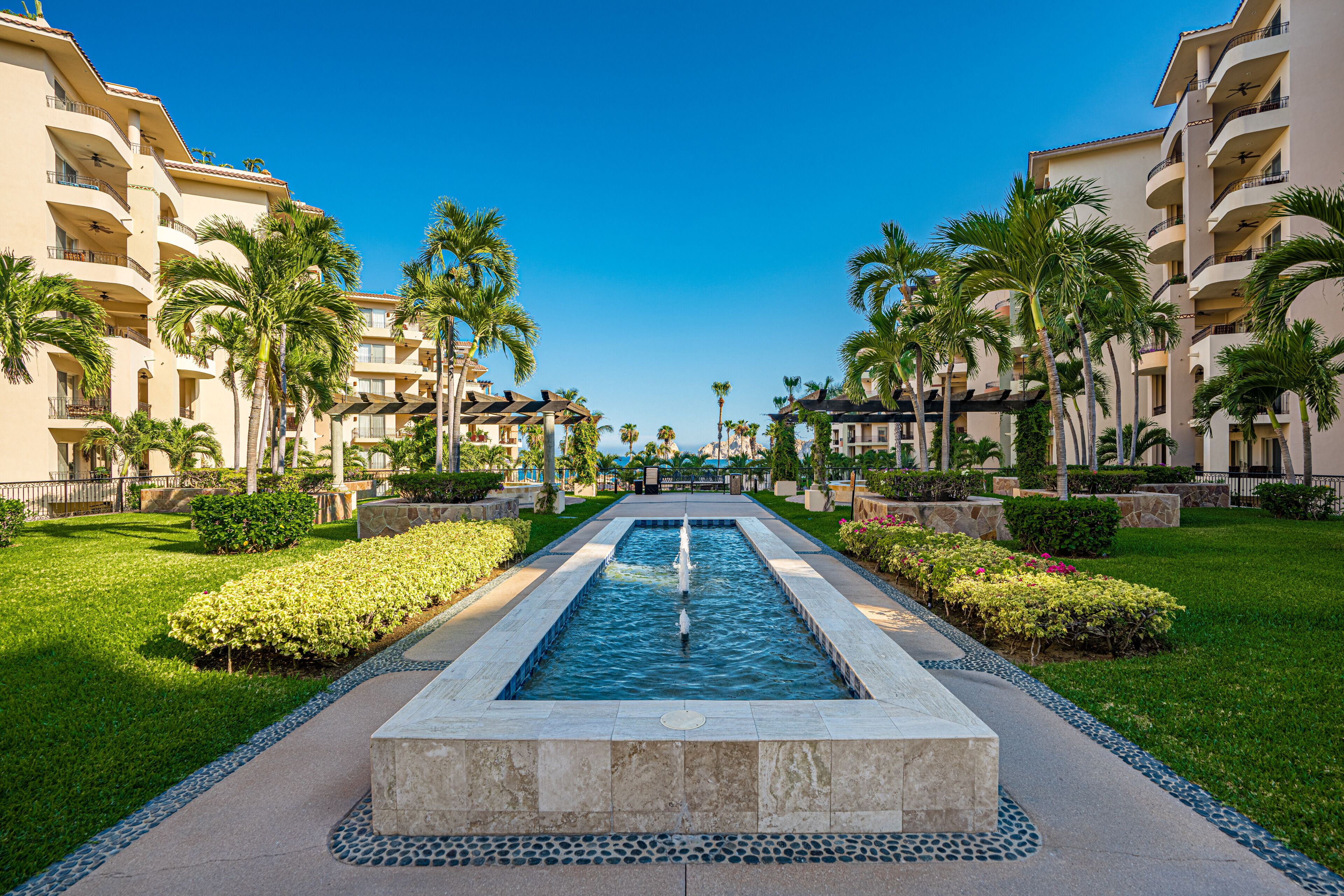A hotel courtyard with a central water feature, surrounded by palm trees and well-maintained lawns.