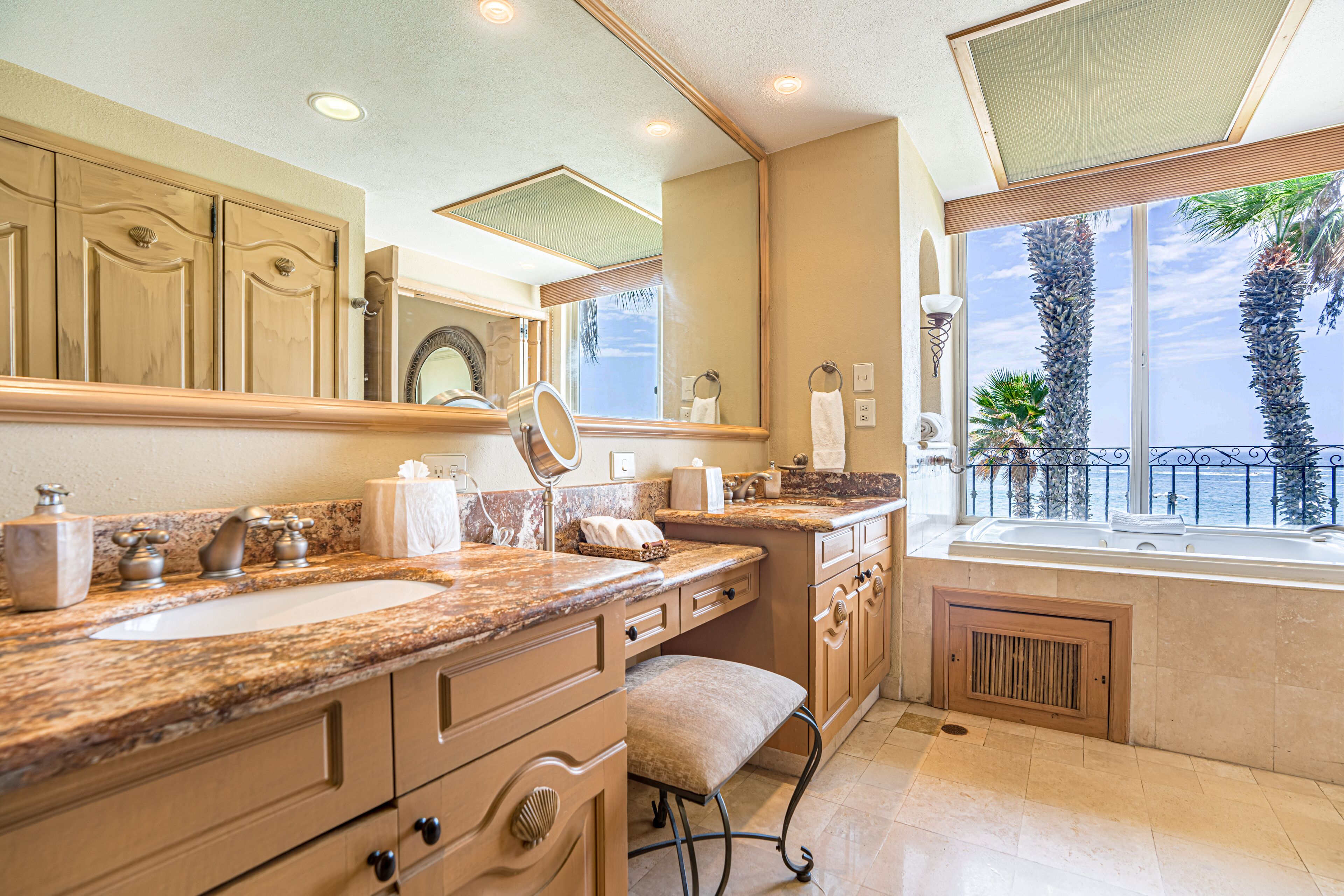 A bathroom with a large sink, vanity, and a window with a view of palm trees and the ocean.