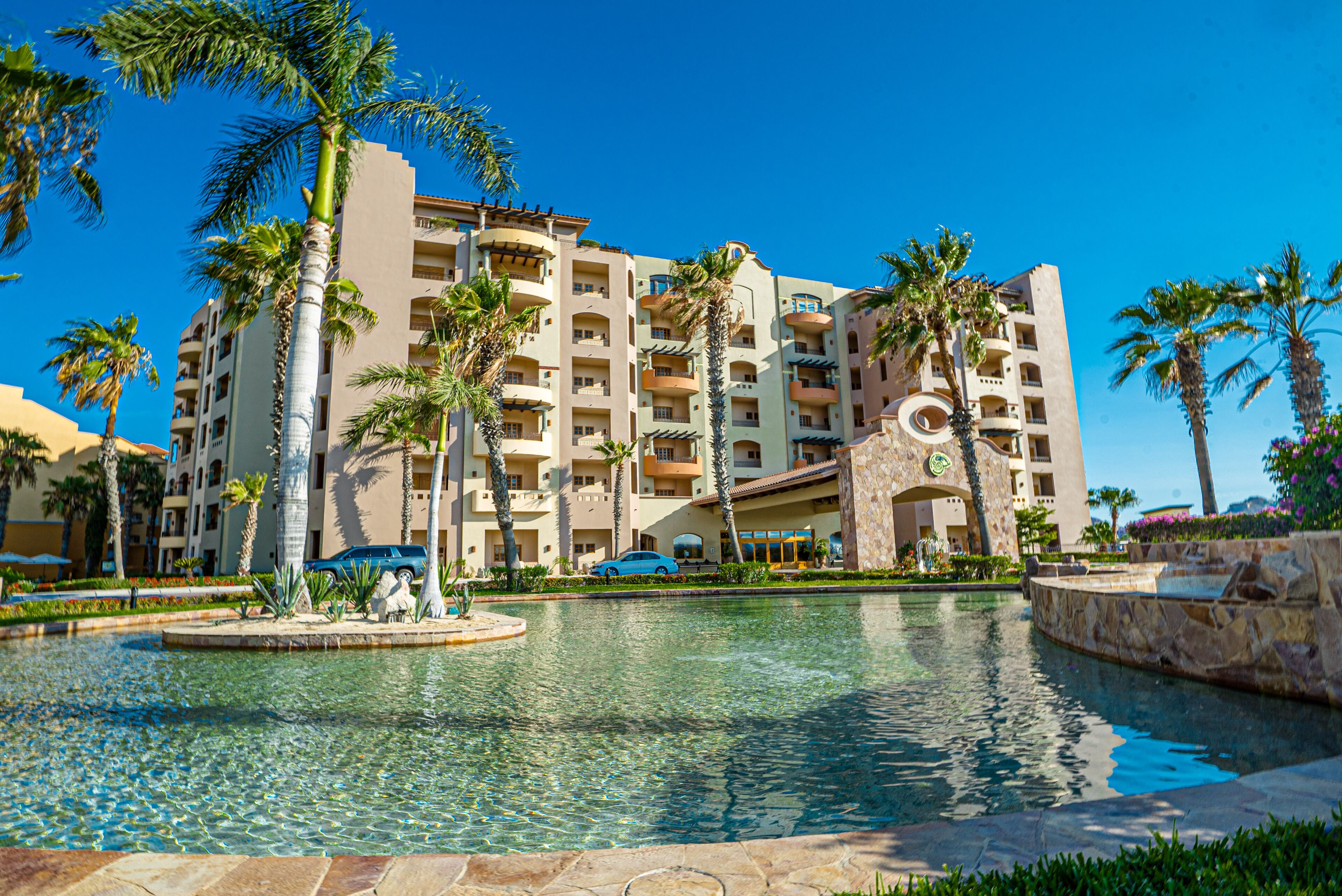 A hotel with multiple floors, a swimming pool, and palm trees.