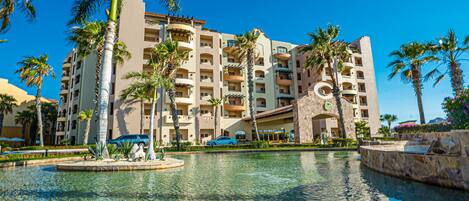 A hotel with multiple floors, a swimming pool, and palm trees.
